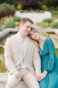 couple sitting by water fountain holding hands and smiling