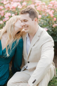 girl kissing boy on cheek in rose garden while they sit in the flowers